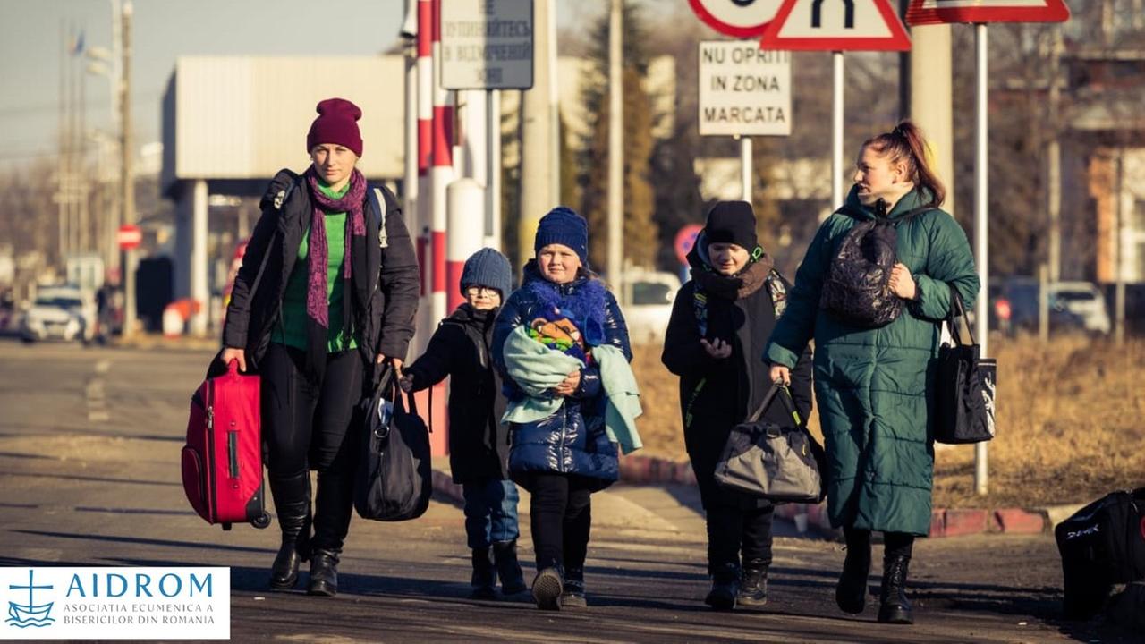 Zwei Frauen und drei Kinder gehen mit vollgepackten Taschen die Straße entlang.