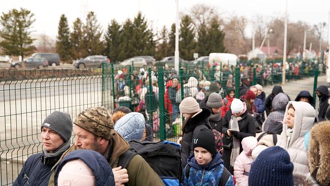 Hunderte Menschen, darunter auch Familien mit Kindern, stehen in Wintermäntel gehüllt entlang eines Zaunes Schlange.