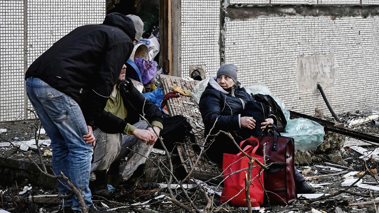 Menschen sitzen vor einem zerstörten Wohnhaus in der Kälte.