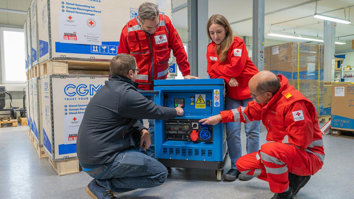 Mitglieder des Österreichischen Roten Kreuzes sehen sich einen blauen Generator an.