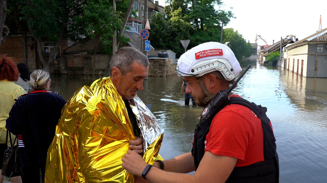 Überschwemmte Straßen. Einem älteren Mann wird von einem Rotkreuz-Mitarbeiter eine Wärmedecke umgelegt.