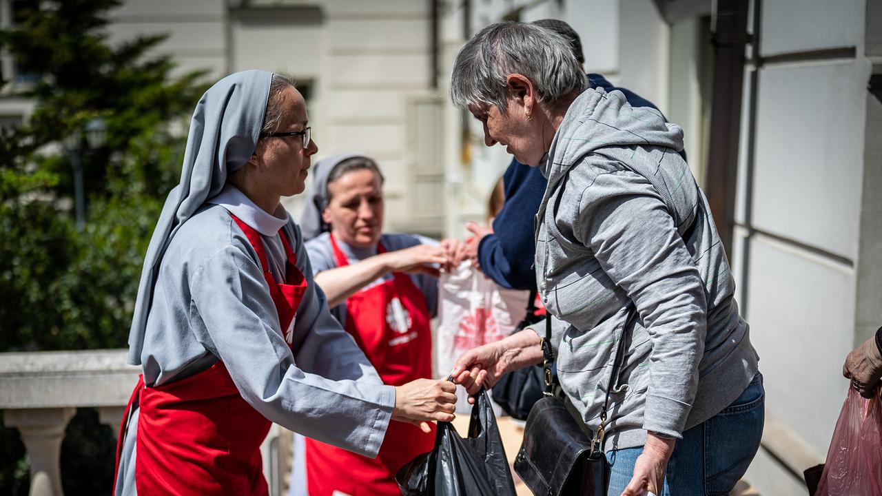 Auf dem Bild sind drei Frauen abgebildet. Zwei Frauen vom Roten Kreuz verteilen Taschen mit Hilfsmittel.
